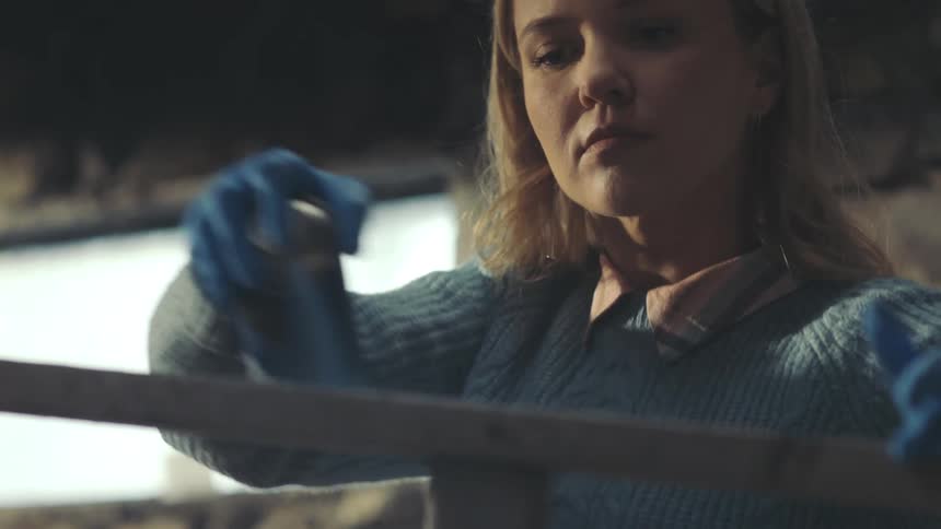 Woman using gloves and blue spray paint to paint a wooden staircase