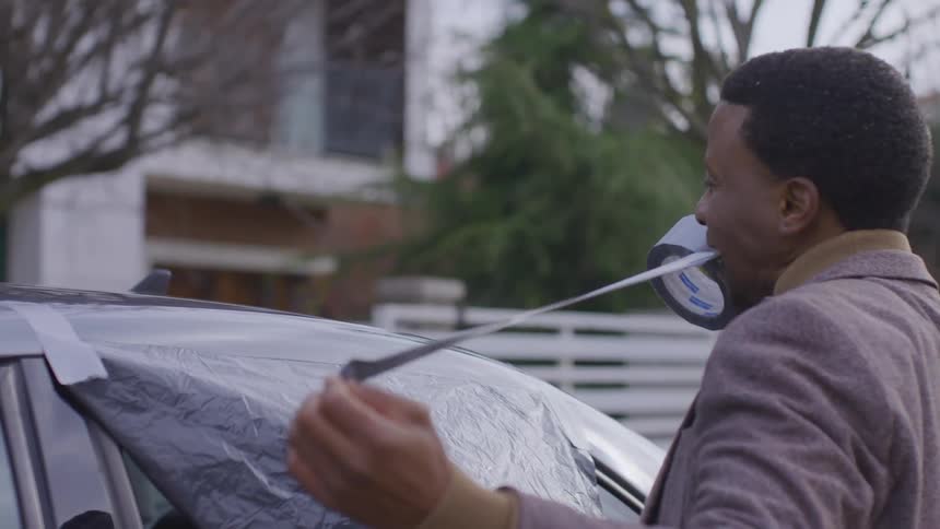Man taping a plastic bag to cover the rear window of a vehicle