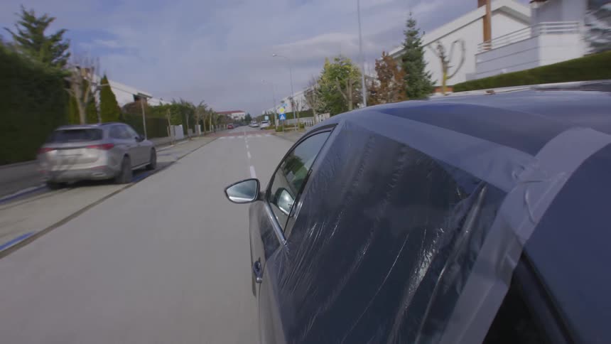Car with broken rear window covered by a plastic bag and traveling through an urban neighborhood
