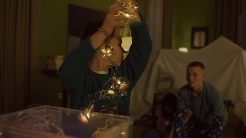 Children taking christmas lights and decorating a cabin out of a sheet