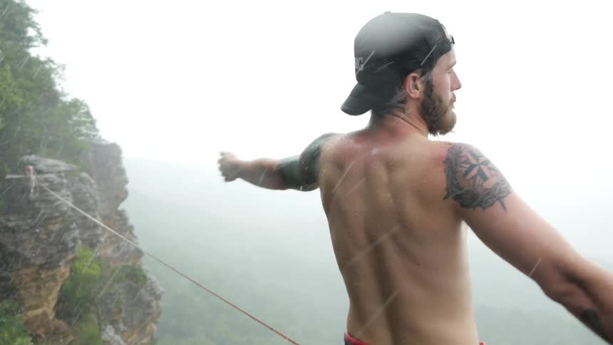 Man stands on a cliff shirtless on a stormy day with heavy rain