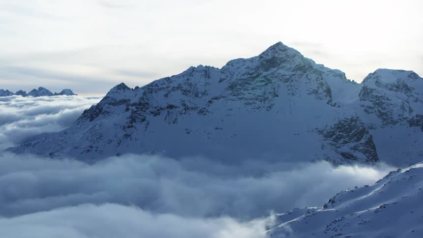 Snowcapped mountain rises above the clouds in the sunlight