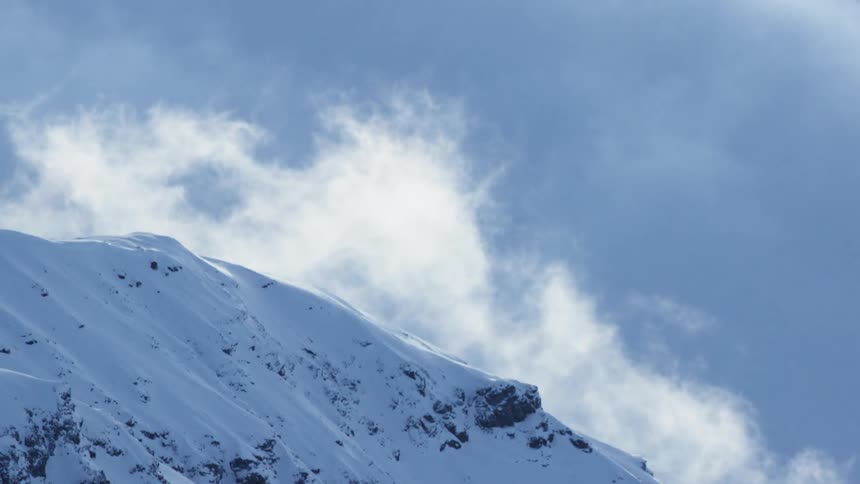 Snow covered mountain peak with clouds in the background and soft sunlight