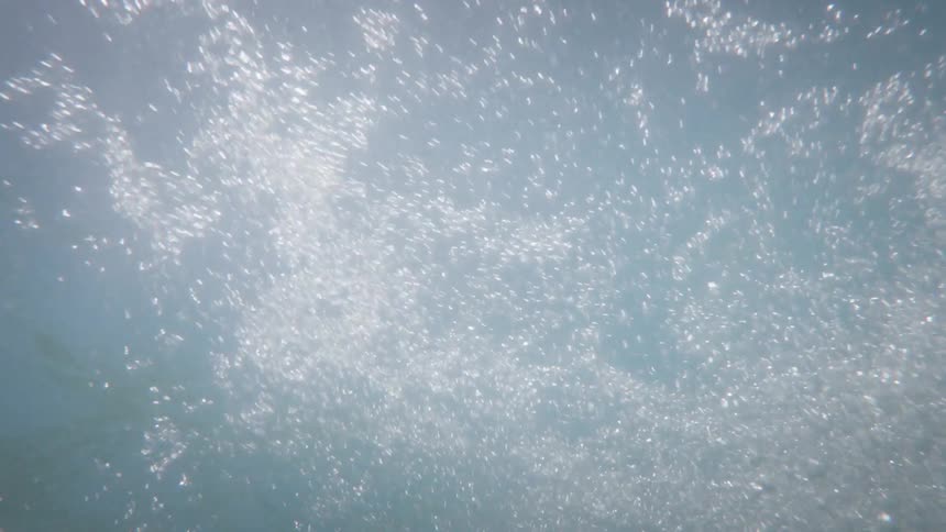 A person jumping into the water creates a trail of air bubbles rising upward underwater