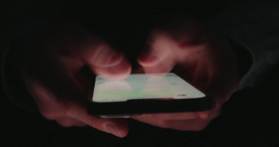 In the dark someones hands are illuminated by a smartphone screen as they type