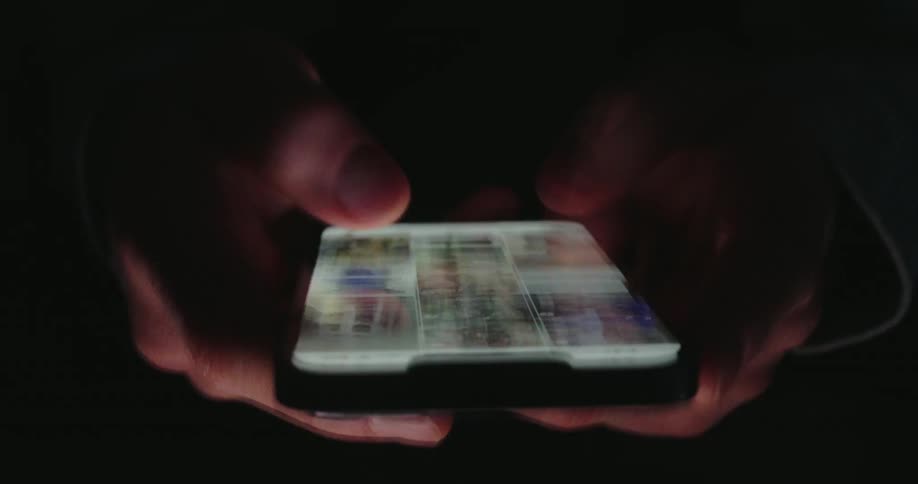 Person holds a smartphone in the dark while browsing a gallery of images on the illuminated screen