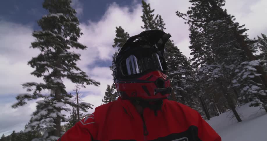 Close up of a person wearing a helmet riding through a snowy area with trees
