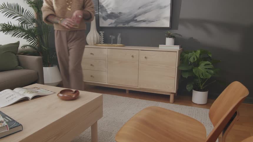 A person taking a glass cup from a wooden rack leaning against a wall in a living room