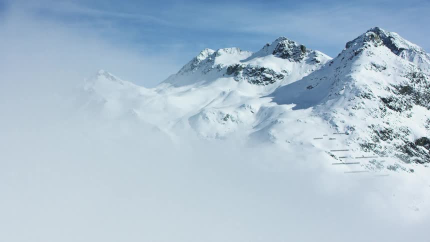 Snowcovered mountain peaks rise above a layer of fog under a clear blue sky