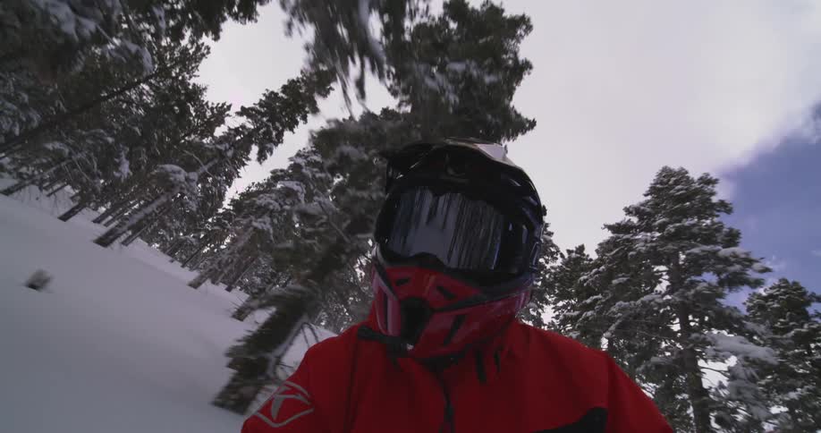 Person wearing a helmet moving at high speed through a snowy mountain with conifers