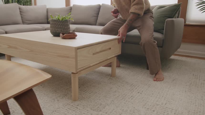 Person sitting on a sofa closing the drawer of a wooden coffee table in a living room