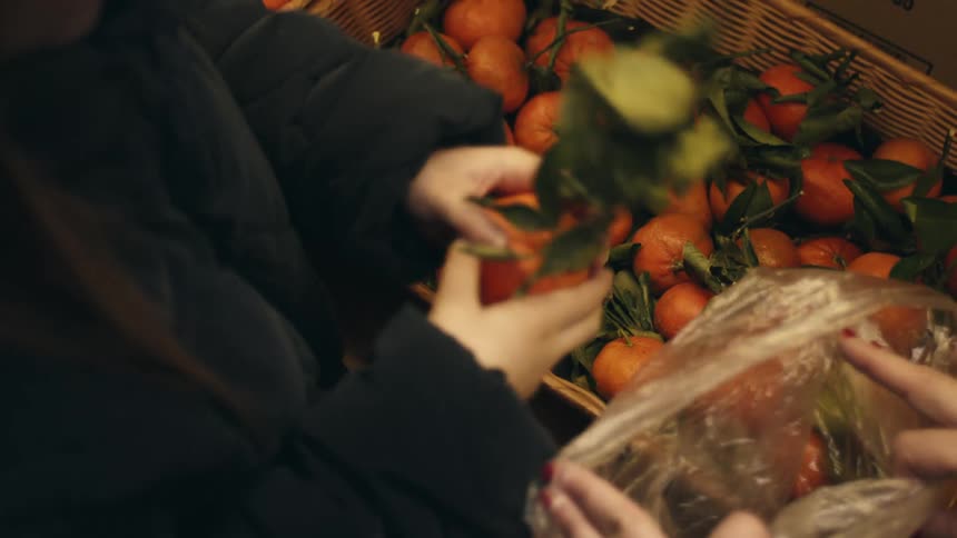 A person is picking oranges from a basket in the grocery store