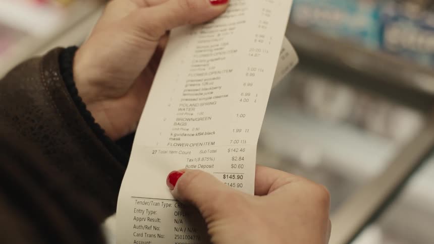 A persons hand with red nails holding a shopping receipt on a white paper with various texts