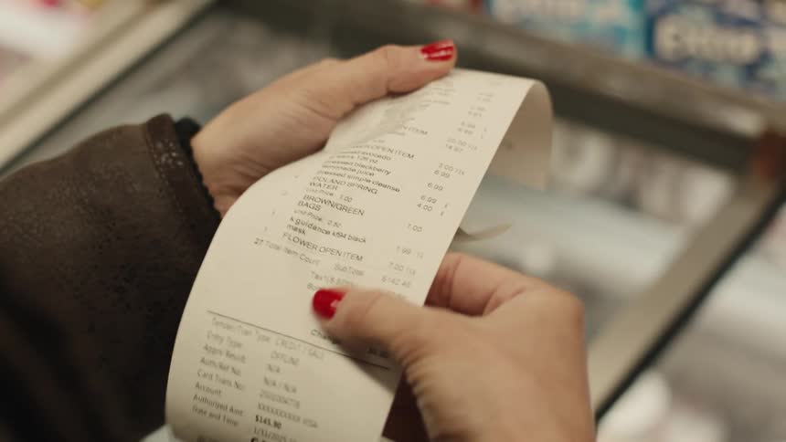A female customer reads a shopping receipt while standing in front of a freezer in a grocery shop