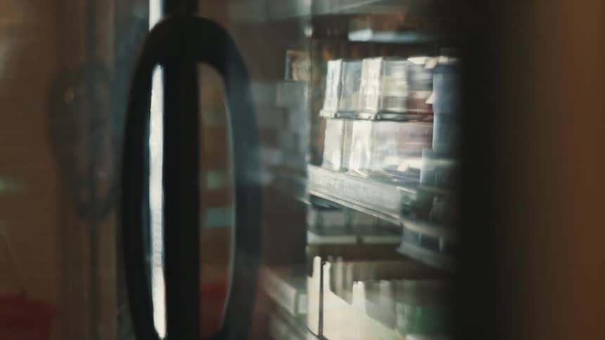 A woman opens a glass door of a display fridge containing groceries in a store
