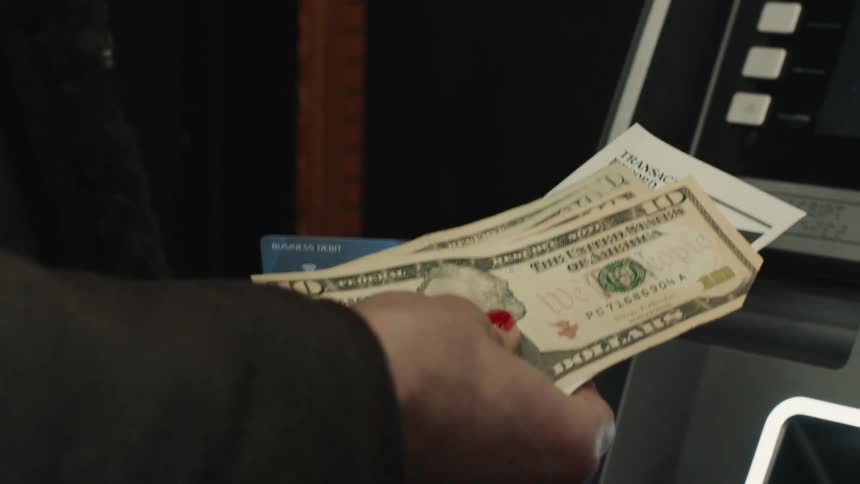 Pair of hands holding money in wallet in front of an atm
