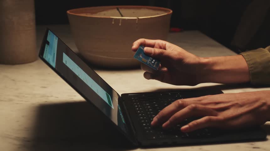 Person holds a credit card while typing on a laptop on a marble table