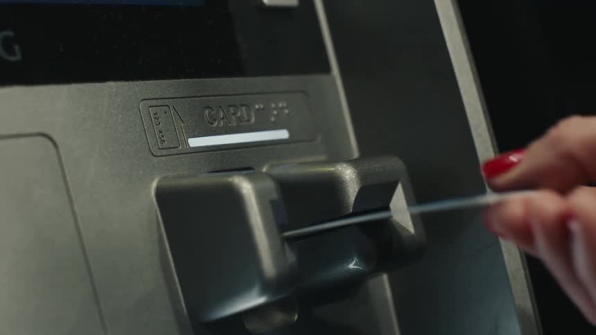 Hand with red painted nails inserting a card into a silver atm