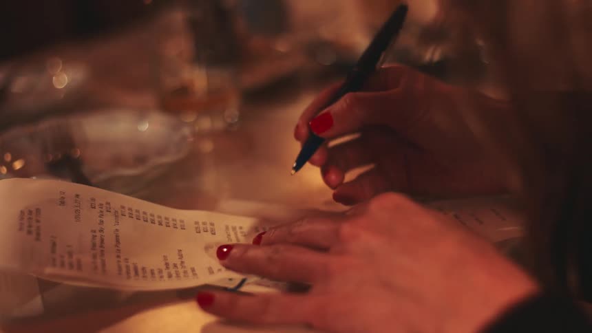 Hands with red nails sign a receipt on the table using a pen