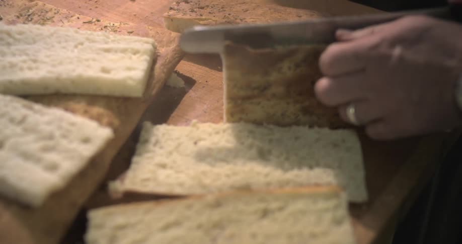 A person is cutting a piece of focaccia bread on a wooden cutting board