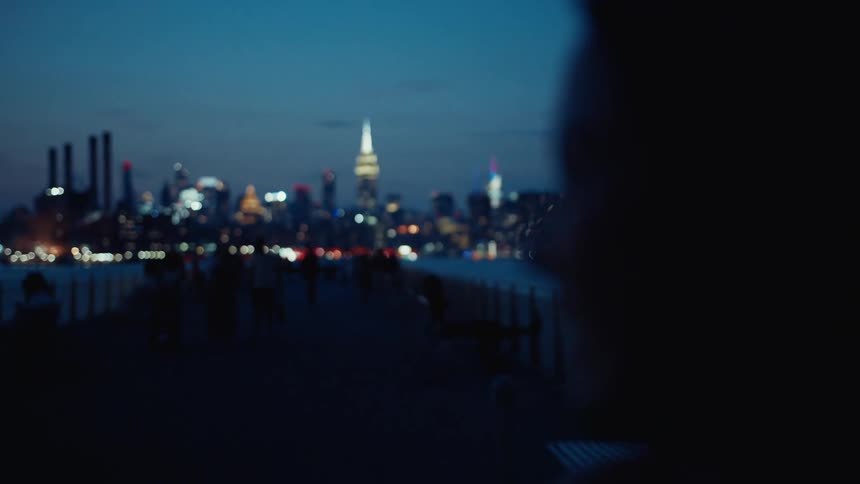 Silhouette of a womans face in an outdoor setting at night with modern skyscrapers on the horizon