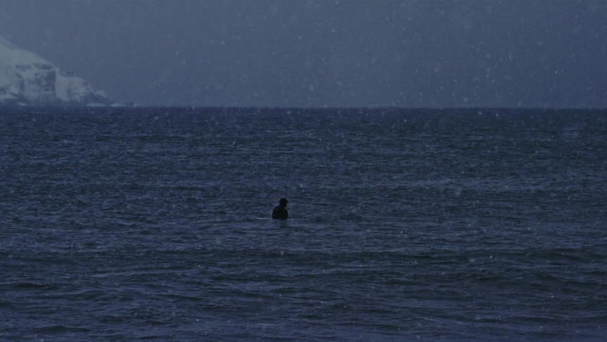 A person is swimming in ocean water as its snowing