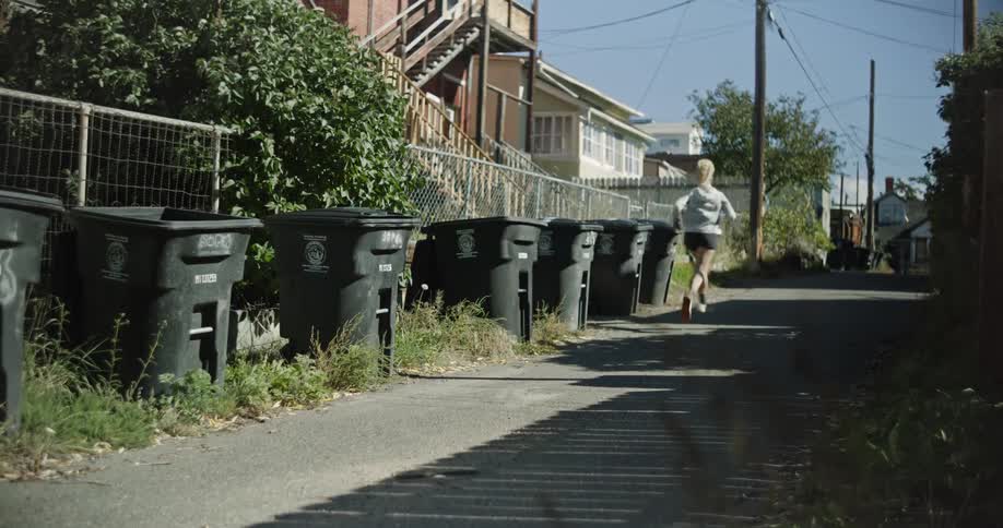 A blonde woman runs down a side street in a residential neighborhood on a sunny summer day