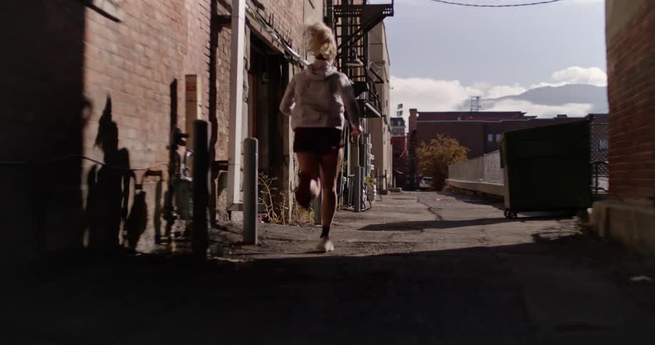 A woman is running down an alleyway lined with buildings on a sunny morning