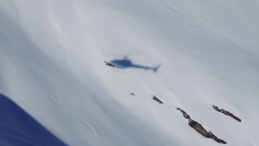 The shadow of a helicopter flying over a completely white snow mountain