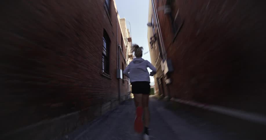 A woman is running down a narrow alleyway between two brick buildings at morning
