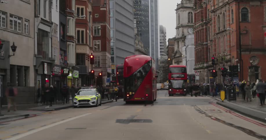 A busy urban street in london with a mix of red doubledecker buses taxis and pedestrians framed by historic and modern buildings