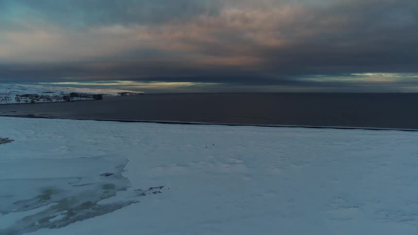 An expansive icy landscape stretches to a dark horizon under a dramatic cloudstreaked sky