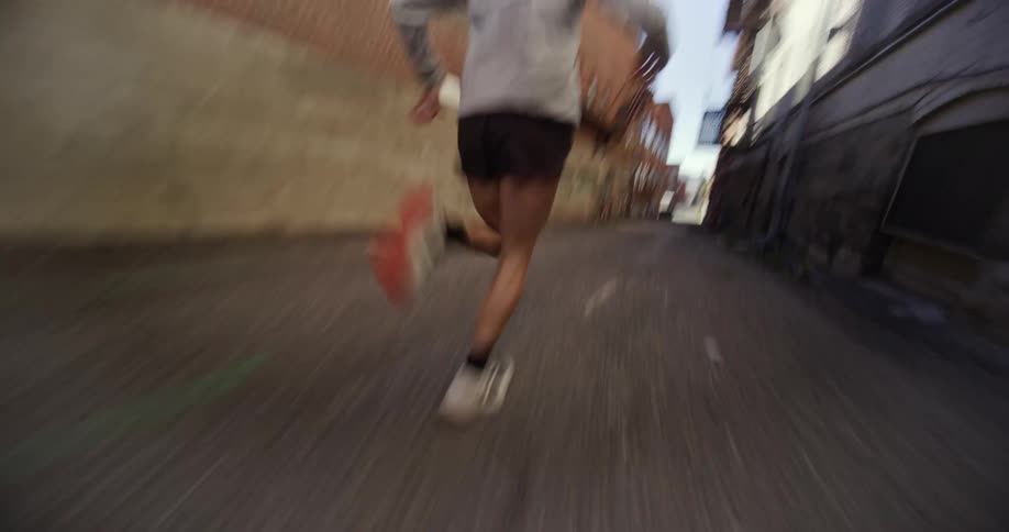 A woman is running down a narrow alleyway between two brick buildings at morning