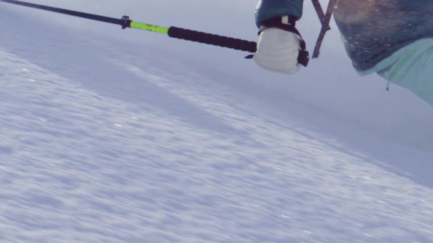 A person is skiing downhill on a snowy slope wearing a blue jacket and light blue pants holding a ski pole in a gloved hand with snow spraying up around the skier