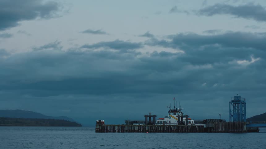 Large boat sits at a dock in the middle of the water under a cloudy sky