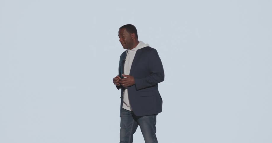 Man walks back and forth during a speech while a camera flashes