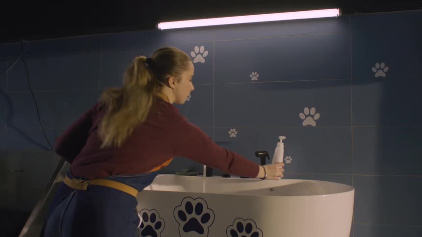 Woman in an apron holds a jar over a white bathtub decorated with paw prints in a blue petthemed space