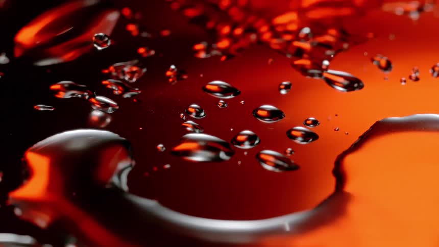 A water droplet falls onto a mirrored surface sending smaller droplets flying and merging with other puddles in a vivid closeup shot