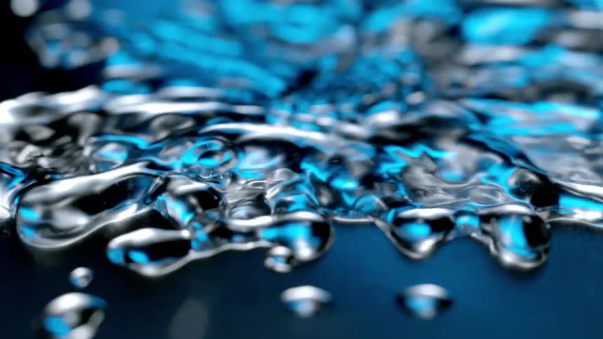 Water drop falls into a small puddle creating a splash that flows over nearby beads of water