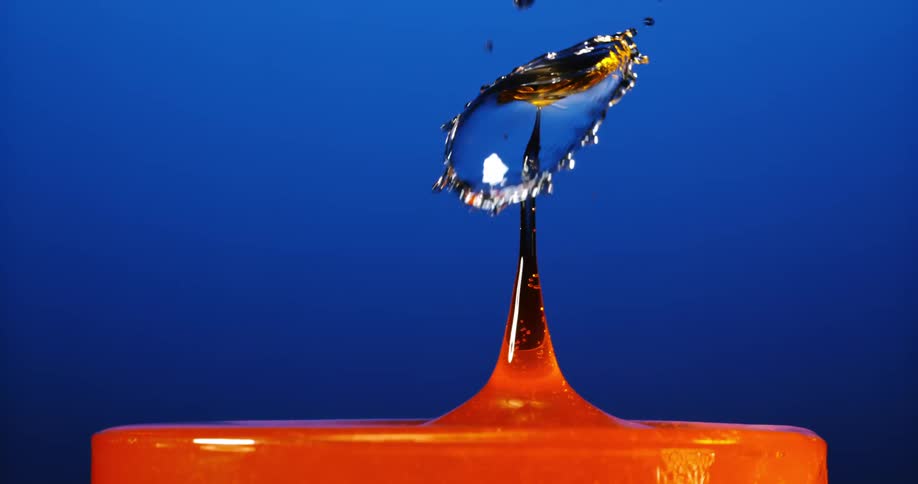 Liquid drops falling in orange liquid against a blue background