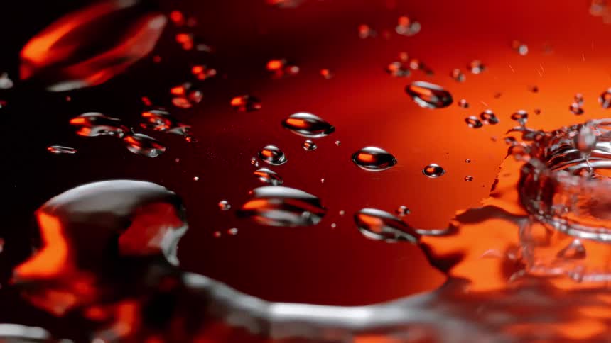 A few drops of water falling on a transparent surface with an orange reflection in the environment and making a splash