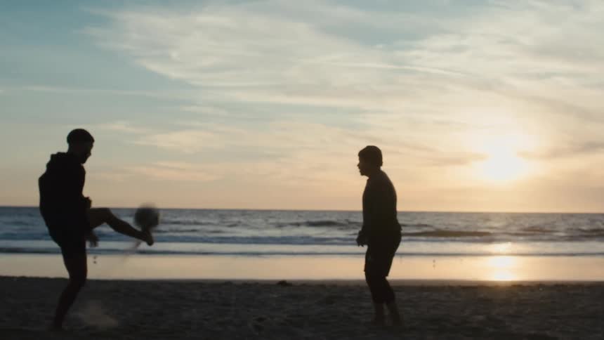 Two men kick the soccer ball back and forth on the beach