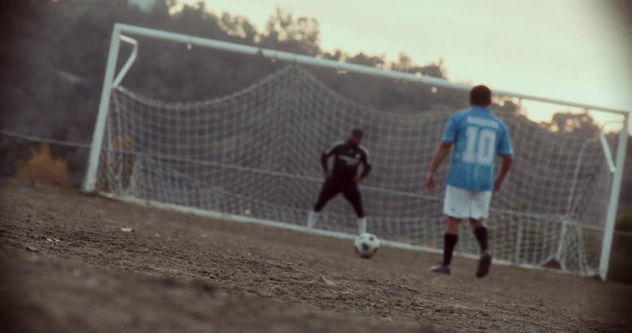 Two men play soccer with one defending the goal on an autumn day