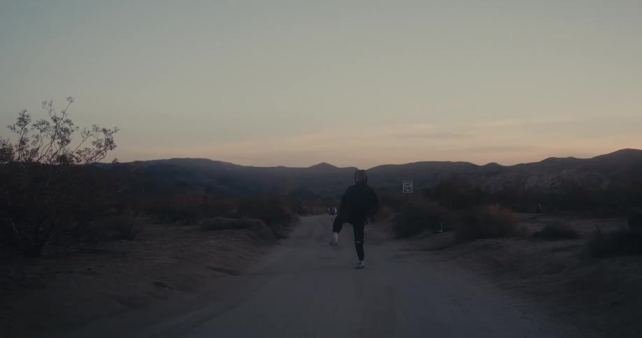 Man kicks around a small ball while standing on a rural road leading towards the hills after dusk