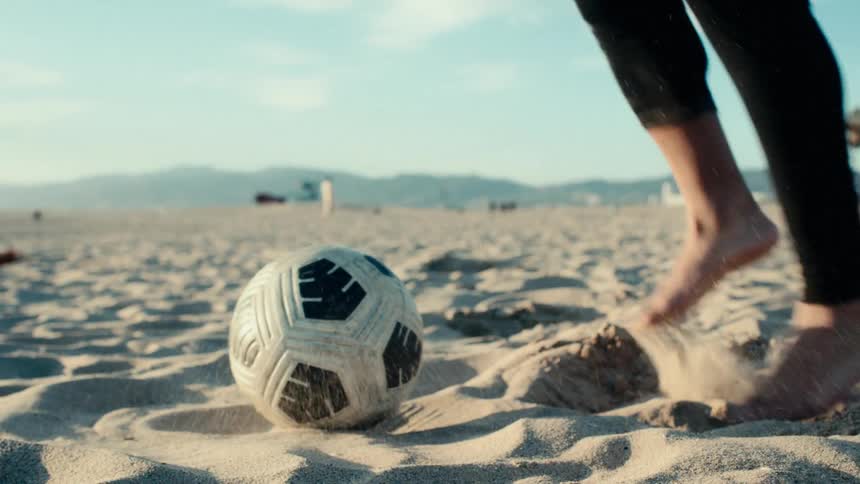 A persons feet are placed on a ball that is on a sand surface