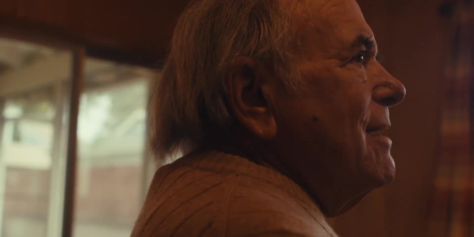 An elderly man sings into a broom handle in his living room at home