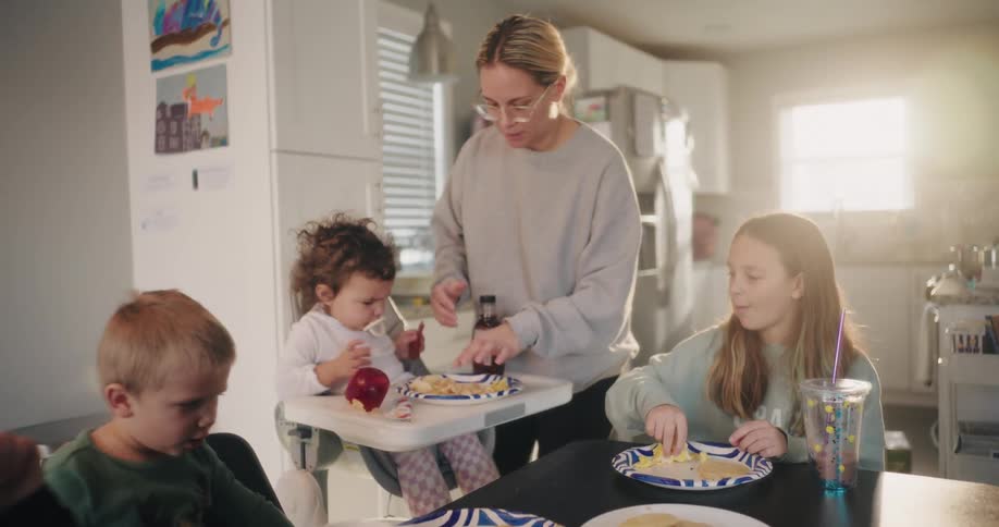 A mother prepares a meal for her three young children at the kitchen table