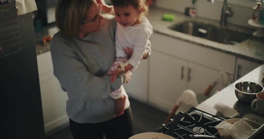 Mother with a baby on her lap cooking in the kitchen