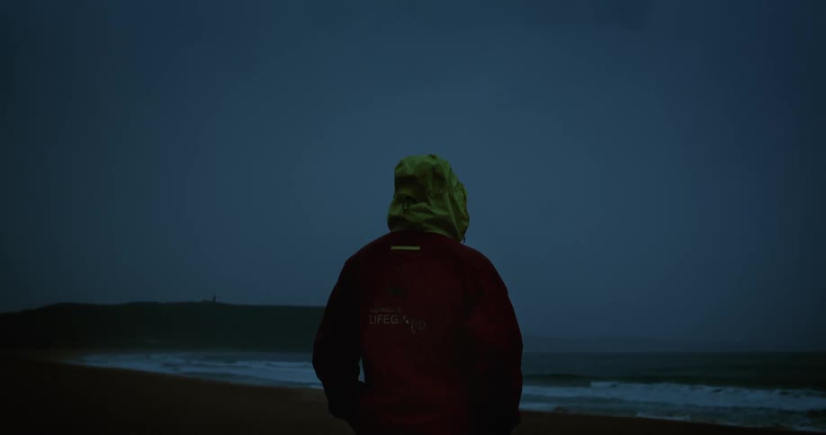 Person in jacket and cap watching the sea at night with thunder