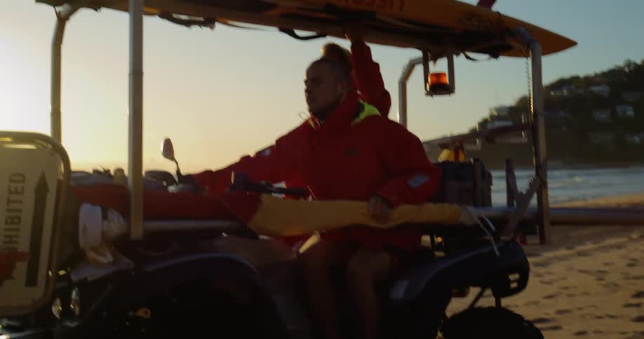 Lifeguard driving a rescue vehicle on the beach at sunset carrying a board and lifesaving equipment
